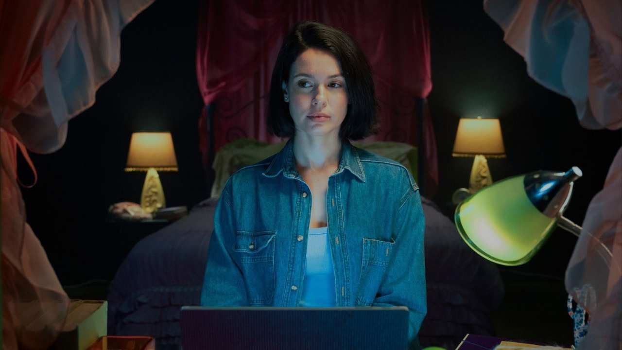 a woman sitting with a laiptaop in front of a bed